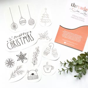 Puede incluir: Una colecci&oacute;n de dise&ntilde;os de bordado navide&ntilde;os en blanco y negro. Incluye adornos, un &aacute;rbol de Navidad, copos de nieve, mitones, un oso y el texto "merry CHRISTMAS". Tambi&eacute;n hay una tarjeta con el texto "threads in zen".