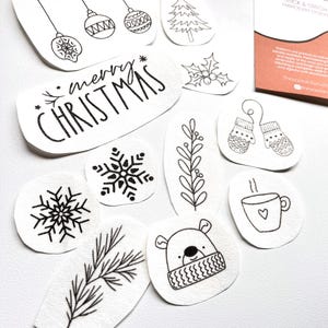 Puede incluir: Una colecci&oacute;n de dise&ntilde;os de bordado blancos troquelados con arte lineal negro. Los dise&ntilde;os incluyen adornos navide&ntilde;os, un &aacute;rbol de Navidad, copos de nieve, un oso con bufanda y el texto "merry CHRISTMAS".