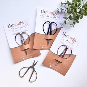 May include: Three packages of embroidery scissors with the text "threads in zen" on the front. The scissors are black, rose gold, and silver.