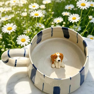 Puede incluir: Una taza de cer&aacute;mica con base color crema y rayas verticales azul oscuro. La taza cuenta con un asa a rayas azules y una peque&ntilde;a figura tridimensional de un perro marr&oacute;n y blanco en el fondo interior. El nombre Eric est&aacute; grabado en el exterior.