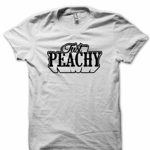 May include: White t-shirt with black text that reads "Just Peachy".
