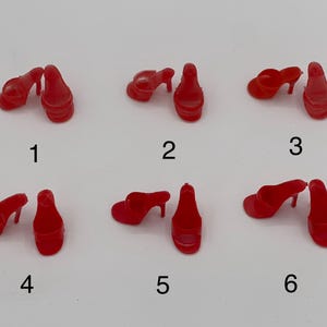 May include: Six pairs of miniature red high-heeled shoes are arranged on a white surface. The shoes are all the same style, with a pointed toe and a thin heel. The shoes are numbered 1 through 6.
