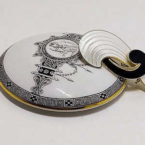 Peut inclure: Broche vintage avec un design en forme d'éventail argenté, rehaussé d'émail noir et de bordures dorées. Repose sur une boîte à bijoux ronde blanche avec une bordure grecque noire et dorée et une illustration en noir et blanc.