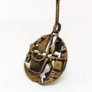 May include: A gold-toned pendant necklace featuring a stylized abstract design. The pendant is shaped like a circle with a textured surface and intricate details.