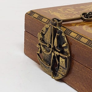 May include: A wooden box with a brass latch shaped like a ship's wheel. The box is decorated with intricate wood inlay.