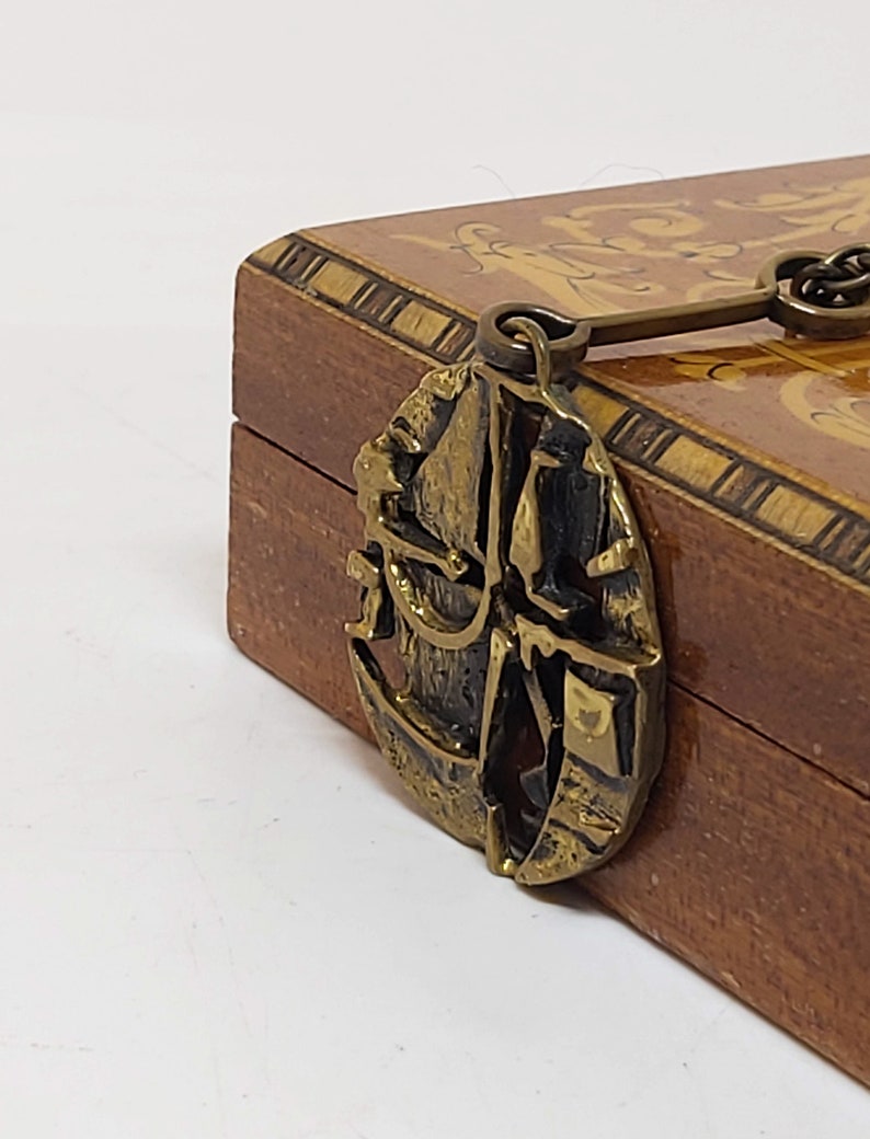 May include: A wooden box with a brass latch shaped like a ship's wheel. The box is decorated with intricate wood inlay.