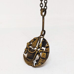 May include: A gold-toned necklace with a pendant featuring a detailed design of a sailboat with a rope and bucket. The pendant is round and has a textured surface.