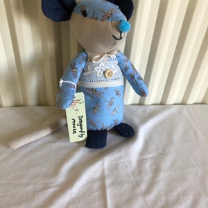 May include: A blue and grey fabric mouse with a dragonfly pattern. The mouse has a blue nose and black ears. The mouse is holding a tag that says "Dragonfly Mouse".