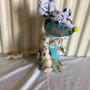 May include: A handmade plush toy mouse with a light blue, yellow and white fabric design. The mouse has a long tail and is holding a tag that says "Dog House".