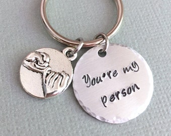 May include: Silver keychain with two charms. One charm features two hands clasped together. The other charm is a round disc with the text "You're my person" engraved on it.