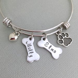 Op de afbeelding: Zilveren armband met een hart, een pootprint en twee beenderen met de namen "Molly" en "Elmo" gegraveerd.
