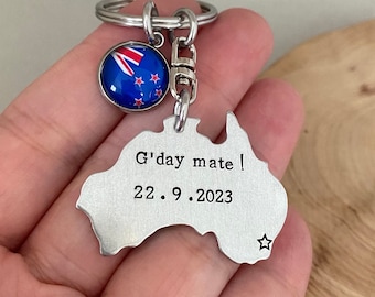 May include: Silver keychain shaped like the outline of Australia with the text "G'day mate! 22.9.2023" and a small star. A small round charm with the New Zealand flag is attached to the keychain.