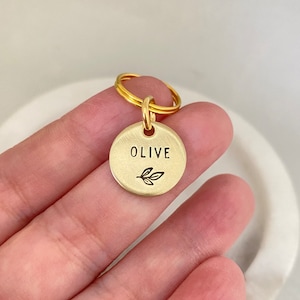 May include: Gold-toned keychain with a round tag that says "OLIVE" with a small olive branch design.