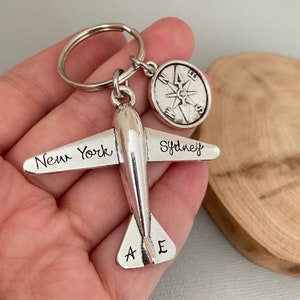 May include: Silver airplane keychain with the words "New York" and "Sydney" engraved on the wings. A compass charm is attached to the keychain.