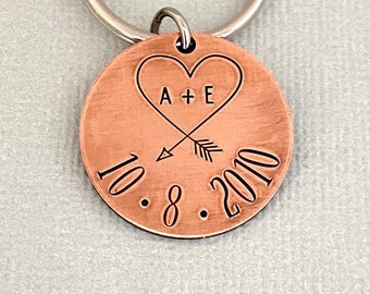 May include: Copper keychain with a heart design and the text "A + E" inside the heart. Below the heart is an arrow pointing to the right and the date "10.8.2010".