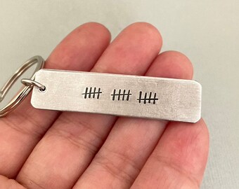 May include: Silver keychain with a rectangular tag engraved with three sets of five hash marks. The keychain has a silver ring.