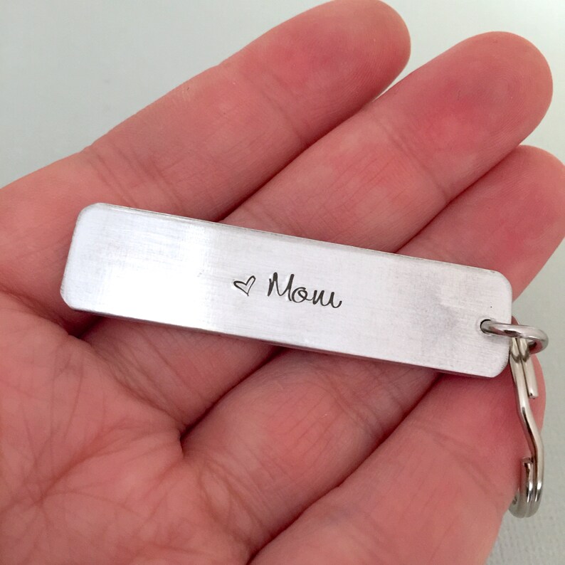 May include: Silver keyring with a rectangular tag engraved with a heart and the word "Mom".