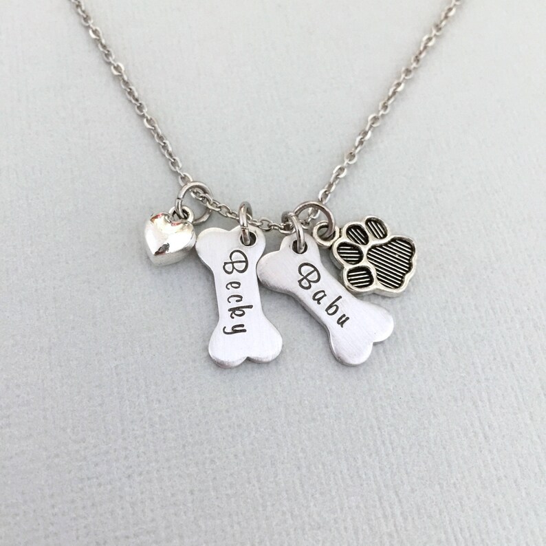 May include: Silver necklace with a heart charm, two bone charms engraved with the names "Becky" and "Babu", and a paw print charm.