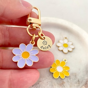 Puede incluir: Llavero dorado con un dije de margarita morada, un dije de margarita blanca, un dije de margarita amarilla y un dije redondo dorado con la palabra "daisy" grabada.