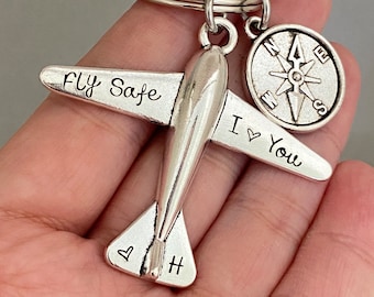 Może przedstawiać: Srebrny brelok do kluczy w kształcie samolotu z wygrawerowanym napisem "Fly Safe I Love You". Brelok zawiera również zawieszkę w kształcie kompasu.