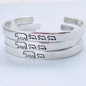 May include: Silver bracelet with a design of a mother bear and her cubs walking in a line. The bracelet is made of three stacked bands.