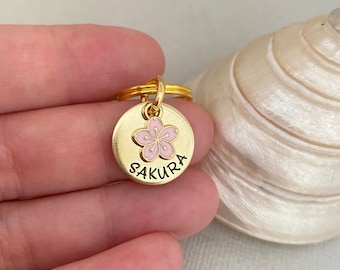 May include: Gold keychain with a pink cherry blossom charm and the word "SAKURA" engraved on the front.