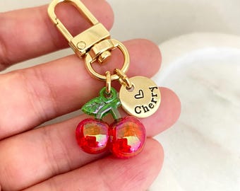 May include: Gold keychain with a red and green cherry charm and a gold charm with the word "Cherry" and a heart symbol.