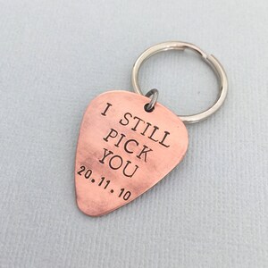 May include: Copper guitar pick keychain with the text "I Still Pick You" and the date "20.11.10" engraved on it.