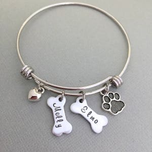 May include: Silver expandable bracelet with charms, including a heart, two bone-shaped charms with the names "Molly" and "Elmo" engraved on them, and a paw print charm.