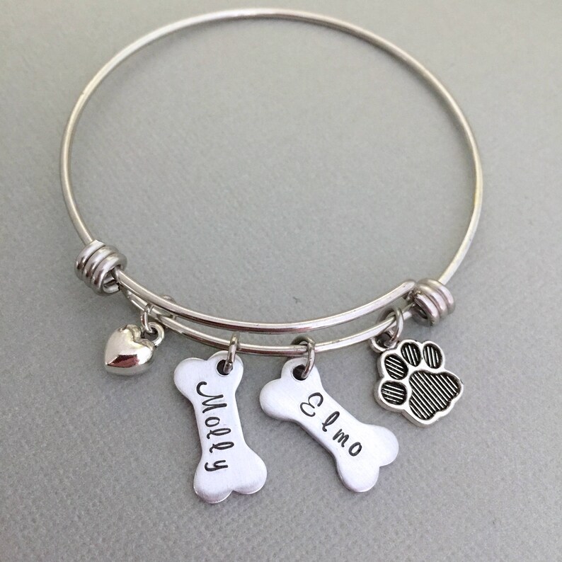 May include: Silver expandable bracelet with charms, including a heart, two bone-shaped charms with the names "Molly" and "Elmo" engraved on them, and a paw print charm.