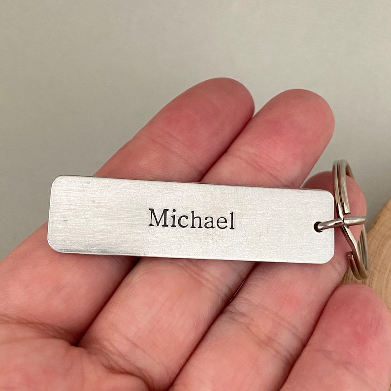 K&ouml;nnte beinhalten: Silberner Schl&uuml;sselanh&auml;nger mit geb&uuml;rsteter Metalloberfl&auml;che und dem eingravierten Namen "Michael".