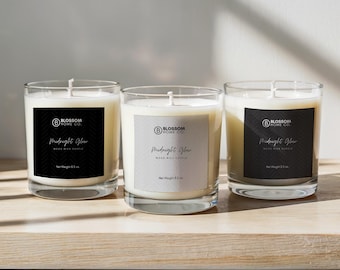 May include: Three glass candle jars with black and white labels. The labels read "Blossom Home Co." and "Midnight Glow Wood Wick Candle". The jars are on a light wood surface.
