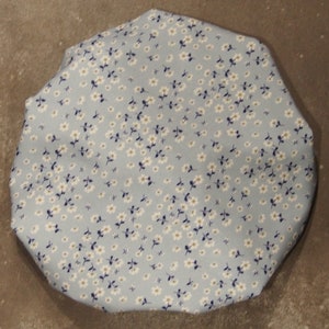 Puede incluir: Un gorro de ducha azul claro con un estampado floral blanco.