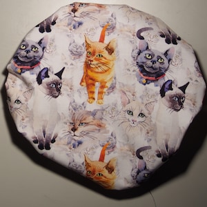 May include: White fabric shower cap with a repeating pattern of watercolour cats in various poses and colours, including orange, grey, and white.