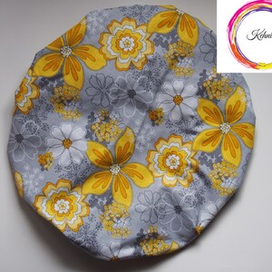 Puede incluir: Un gorro de ducha gris con un estampado floral amarillo y blanco.