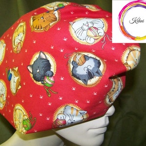 Puede incluir:  gorro de trabajo rojo de tela con un patrón de gatos jugando con ovillos de lana. Los gatos son de varios colores y poses, y el fondo es una tela roja con huellas de patas blancas.