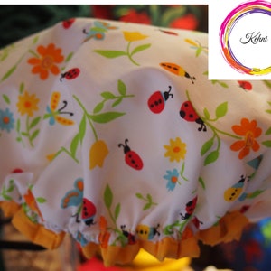 Puede incluir:  gorro de ducha blanco con un patrón floral amarillo, naranja, rojo y verde con mariquitas. El gorro de ducha tiene una banda elástica amarilla.