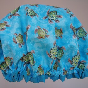 Puede incluir: Un gorro de ducha azul con un patrón de tortugas marinas sobre un fondo azul.