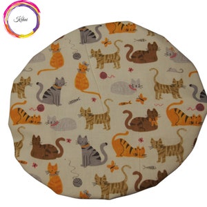 Puede incluir: Un gorro de ducha de tela beige con un patrón repetido de gatos naranja, marrón y gris. Los gatos están en varias poses, incluyendo sentados, de pie y tumbados. Algunos gatos tienen un lazo rosa en el cuello.