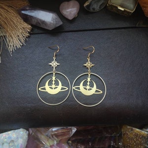 May include: Gold tone earrings featuring a crescent moon and star design. The earrings are drop earrings and have a circular shape.