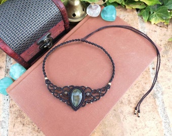 Puede incluir: Un collar de cordón negro con un colgante de piedra verde en forma de lágrima. El colgante está rodeado por un delicado diseño de metal plateado. El collar está atado con un simple nudo.