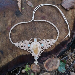 May include: A beige macrame necklace with a large, yellow-brown gemstone pendant and smaller turquoise stones. The necklace is tied with a simple knot and has a delicate, bohemian style.
