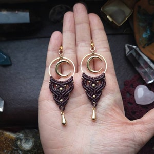 May include: A pair of maroon and gold earrings with a crescent moon charm and a macrame design.