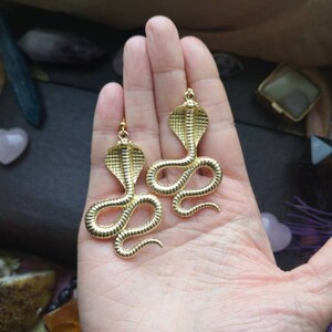 May include: A pair of gold-tone snake earrings. Each earring features a detailed cobra design with a raised, textured surface.