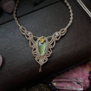 Puede incluir: Un delicado collar de macram&eacute; con un colgante de piedra de labradorita verde. El collar est&aacute; hecho con cord&oacute;n blanco y tiene un acento dorado.