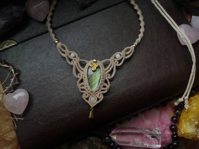 Puede incluir: Un delicado collar de macram&eacute; con un colgante de piedra de labradorita verde. El collar est&aacute; hecho con cord&oacute;n blanco y tiene un acento dorado.