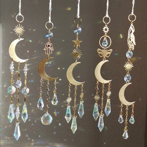 Könnte beinhalten: Fünf goldene Halbmond-Sonnenfänger mit Kristallperlen und tropfenförmigen Prismen, die daran hängen. Jeder Sonnenfänger hat einen anderen Anhänger, darunter eine Hamsa-Hand, einen Stern, eine Sonne, eine Biene und einen Schmetterling.