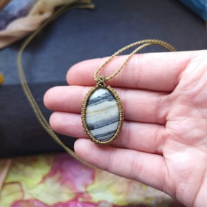 Könnte beinhalten: Eine braune Schnurkette mit einem ovalen Anhänger in Weiß und Schwarz. Der Anhänger ist aus einem Naturstein mit einem einzigartigen Muster.