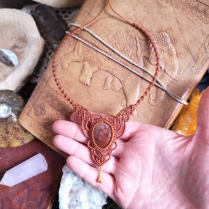 Puede incluir: Un collar de cord&oacute;n de cuero marr&oacute;n con un dise&ntilde;o anudado y un gran colgante redondo de piedra marr&oacute;n.