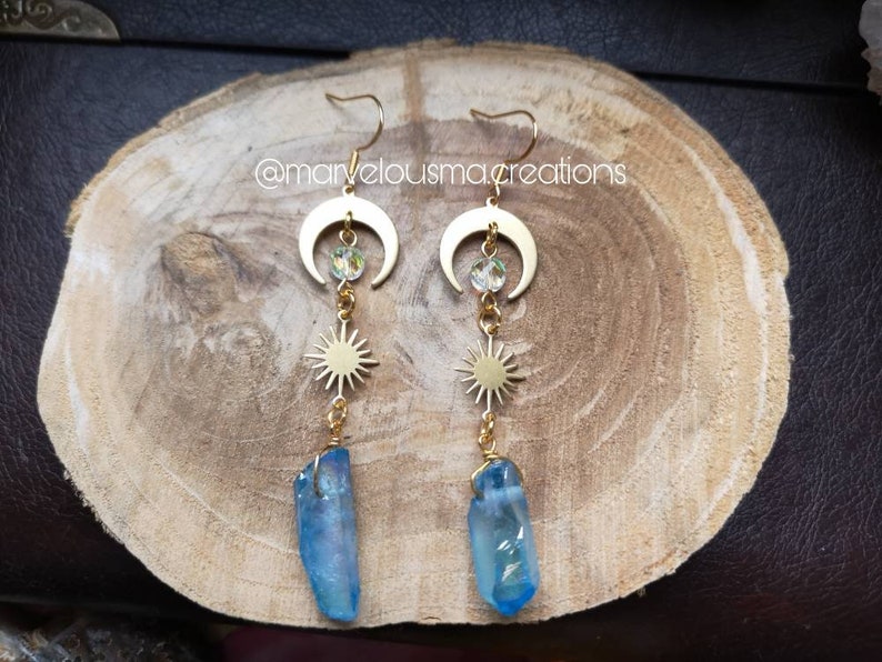 K&ouml;nnte beinhalten: Goldene Ohrringe mit einem Halbmond, einem Stern und einem blauen Kristall-Anh&auml;nger. Die Ohrringe liegen auf einer Holzoberfl&auml;che. @marvellousmacreations